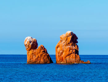 Rock formations in sea against clear blue sky