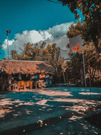 Street by trees and houses against sky