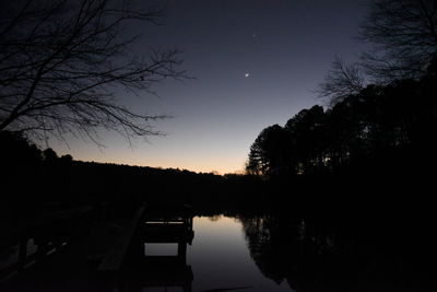 Silhouette trees by lake against sky at sunset