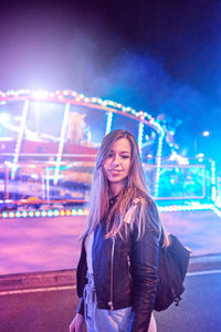 Woman standing against illuminated wall at night