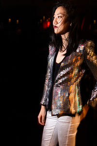 Confident asian female in festive wear standing among shining lights at night party and looking away