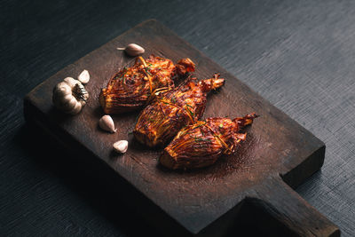 High angle view of chicken meat with garlic cloves served on wooden tray