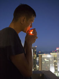 Side view of man smoking cigarette against sky at night