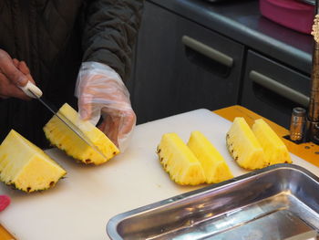 Cropped image of chef wearing gloves cutting pineapple at table