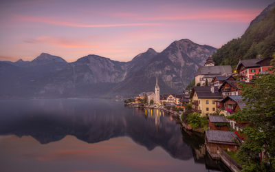 Lake by buildings against sky during sunset