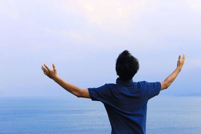 Rear view of man standing by sea against sky