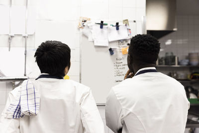 Rear view of multiracial chefs brainstorming over whiteboard in kitchen of restaurant