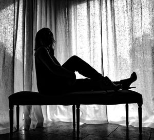 Side view of silhouette woman relaxing on seat against curtain at home