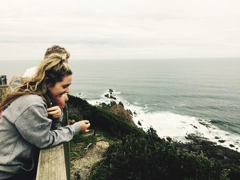 Young woman standing by railing against sea