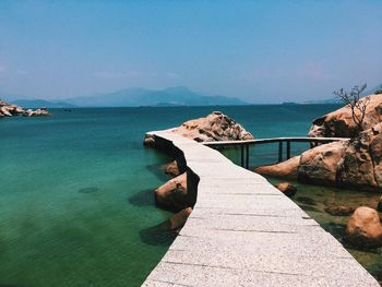 Narrow jetty over sea against sky