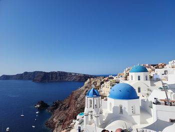 Buildings by sea against clear blue sky