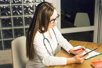 Doctor using digital tablet while sitting by table