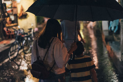 Rear view of people holding wet glass in city during rainy season