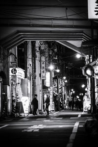 People walking on illuminated road amidst buildings at night