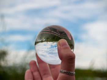 Cropped hand holding crystal ball against sky