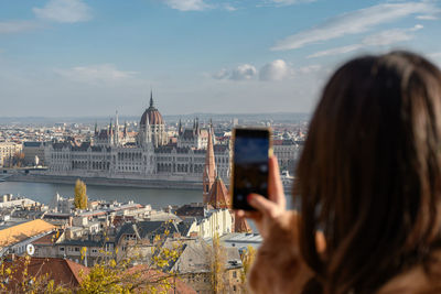Rear view of woman using mobile phone, taking photos of beautiful cityscape of budapest in hungary