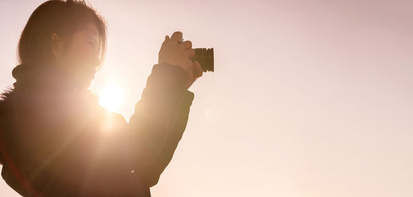 Woman photographing with camera standing against clear sky