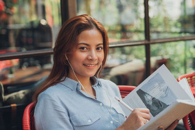 Portrait of smiling young woman writing in book at cafe
