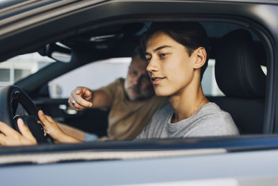 Contemplative young man learning to drive with father while sitting in car