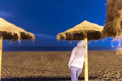 Rear view of man standing at beach against blue sky