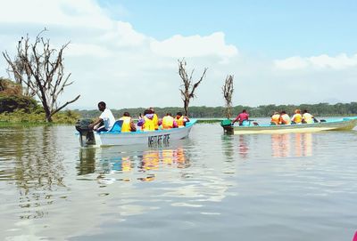 People sitting in boats on lake against sky