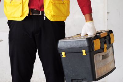 Midsection of carpenter holding toolbox against wall