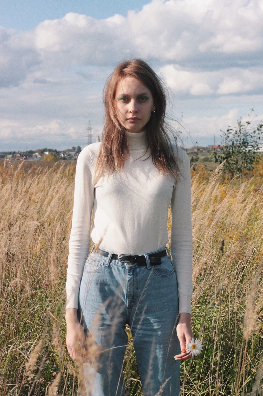 PORTRAIT OF YOUNG WOMAN STANDING ON FIELD