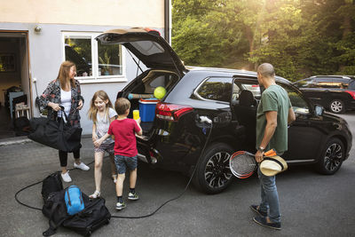 Family with luggage and black electric car in back yard