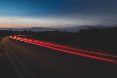 Light trails on road against sky at sunset