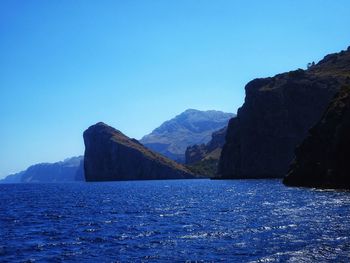 Scenic view of sea and mountains against clear blue sky