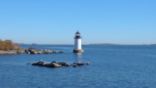 Lighthouse by sea against blue sky