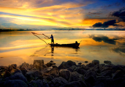 Silhouette man on rock in sea against sky during sunset