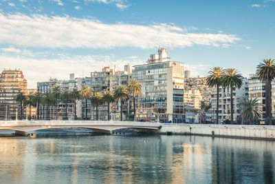 Buildings by river against cloudy sky