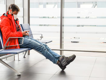 Full length of young man wearing mask sitting on airport