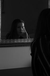 Portrait of young woman looking through window at home