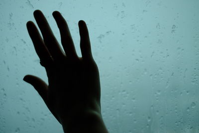 Close-up of hand touching wet window