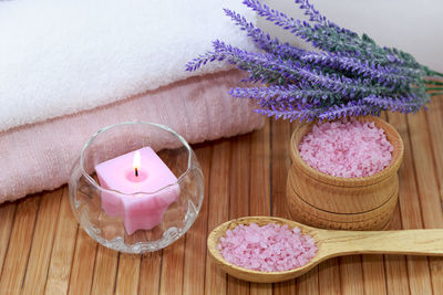 Candle with salts and flowers by towel on table