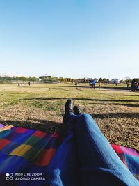 Low section of people relaxing on field against clear sky