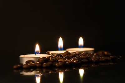 Close-up of lit tea light candles by roasted coffee beans against black background