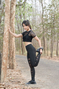 Full length of woman standing by tree trunk in forest