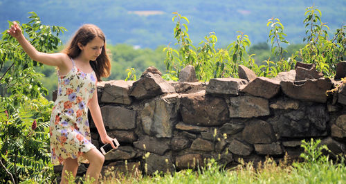 Teenage girl walking on field against stone wall