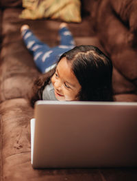 Cute girl using laptop while lying on sofa at home