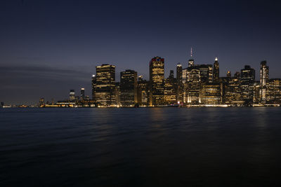 Illuminated buildings by river against sky at night