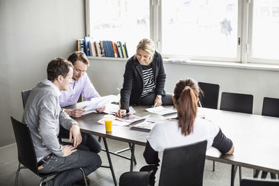 Mid adult businesswoman looking at photographs while discussing on table with colleagues in office