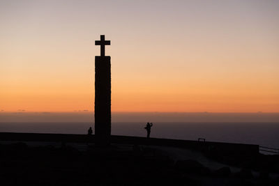 Silhouette of lighthouse at sea during sunset