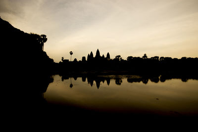 Silhouette temple by river against sky