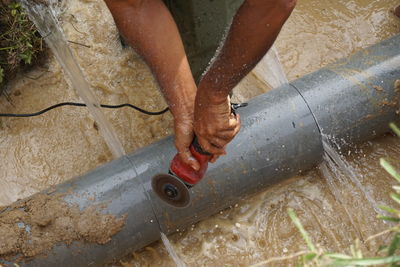 Cropped hands of man cutting water pipe on floor