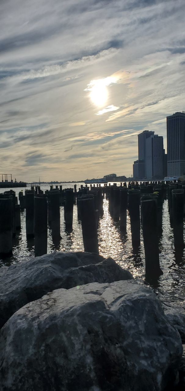 water, architecture, sky, built structure, sunset, building exterior, city, nature, sea, cloud - sky, no people, reflection, building, waterfront, office building exterior, rock, urban skyline, skyscraper, outdoors, cityscape, wooden post