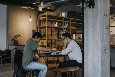 Male business colleagues playing chess on table at office cafeteria