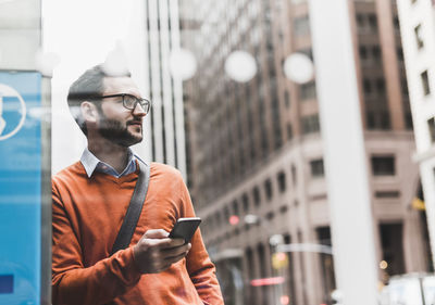 Usa, new york city, businessman leaning on atm holding smart phone